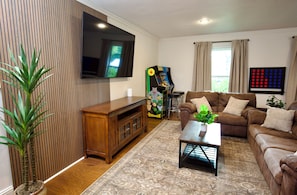 Una sala de estar con una televisión de pantalla plana, un sofá marrón, una mesa de centro, un mueble de madera y una planta.