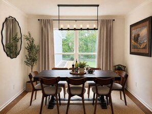 A dining room with a large table, six chairs, a chandelier, a window with curtains, and a framed picture on the wall. - Minutes to MSU| 4BR| Games| EV Charger| Fire Pit (Starkville)
