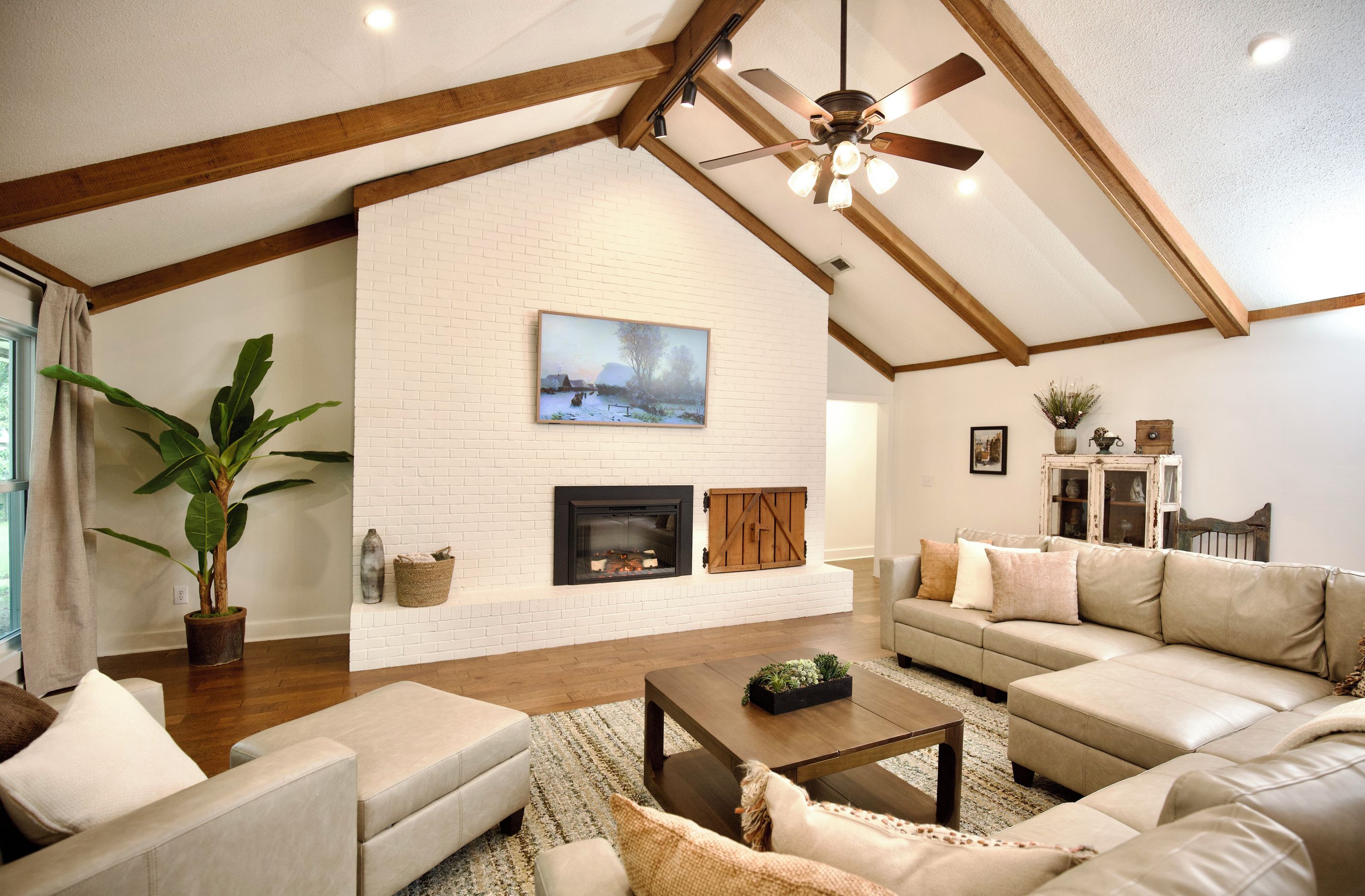A living room with a fireplace, a ceiling fan, and a large window.