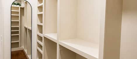 Et walk-in closet med åbne hylder, et spejl og en trægulv.