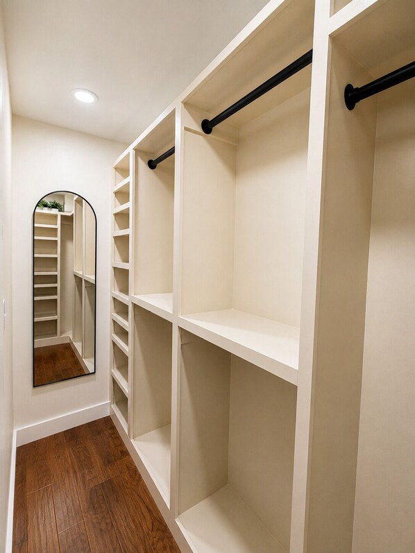A walk-in closet with open shelving, a mirror, and a wooden floor.