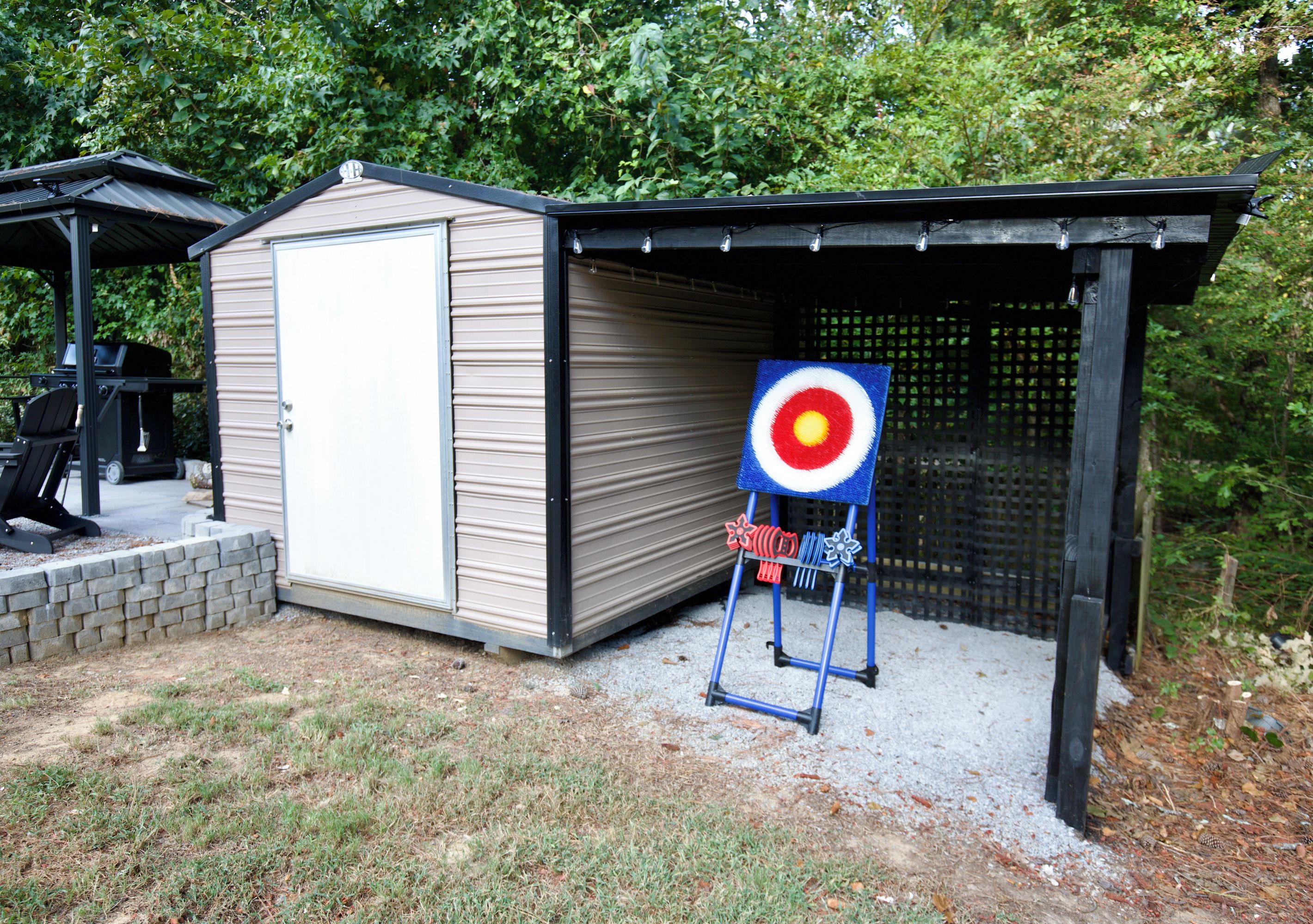 A target board with a bullseye, a shed, and a patio area with a grill.