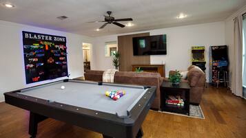 A living room with a pool table, a television, and arcade games.