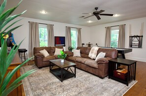 A living room with a brown sofa, a coffee table, a ceiling fan, and a window with curtains.
