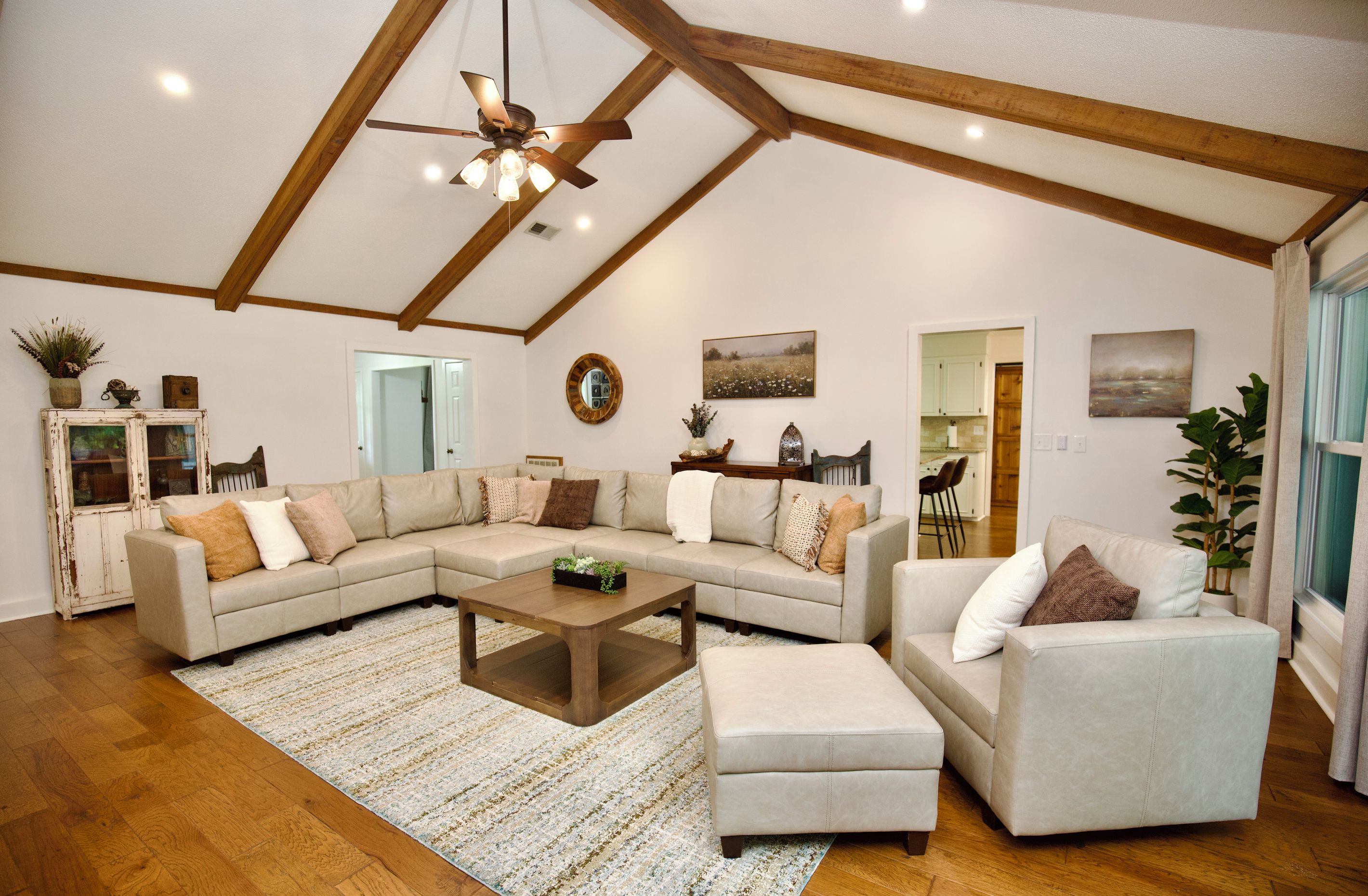 A spacious living room with a large L-shaped sectional sofa, a wooden coffee table, and a ceiling fan.