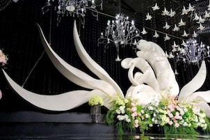 Un escenario con una gran escultura blanca, arreglos florales e iluminación colgante.