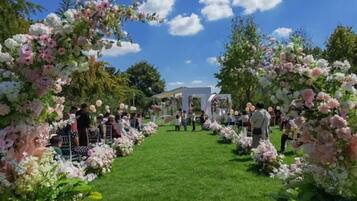 An outdoor wedding venue with a grassy pathway flanked by floral arches.