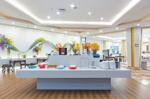 Un vestíbulo moderno de hotel con mostrador de recepción, plantas decorativas y un interior limpio y bien iluminado.