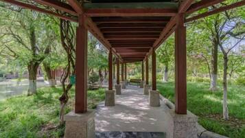 A covered walkway with stone pillars, surrounded by greenery and trees.