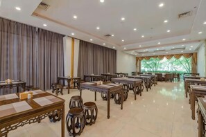 Une salle à manger d’hôtel spacieuse, dotée de nombreuses tables et chaises, d’une grande fenêtre avec des rideaux et d’un sol carrelé impeccable.
