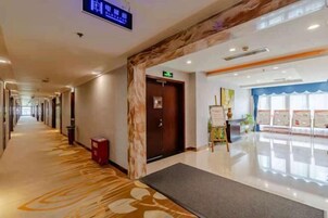 Un pasillo de hotel con mostrador de recepción, un cartel digital y piso alfombrado.