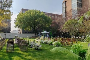 Un espacio al aire libre con sillas y mesas, rodeado de vegetación y un edificio al fondo.