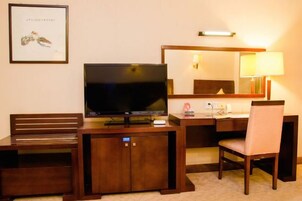 Una habitación de hotel con televisión, escritorio, silla y un cuadro en la pared.