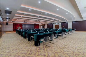A conference room with rows of tables and chairs, a patterned carpet, and a curved ceiling with recessed lighting.