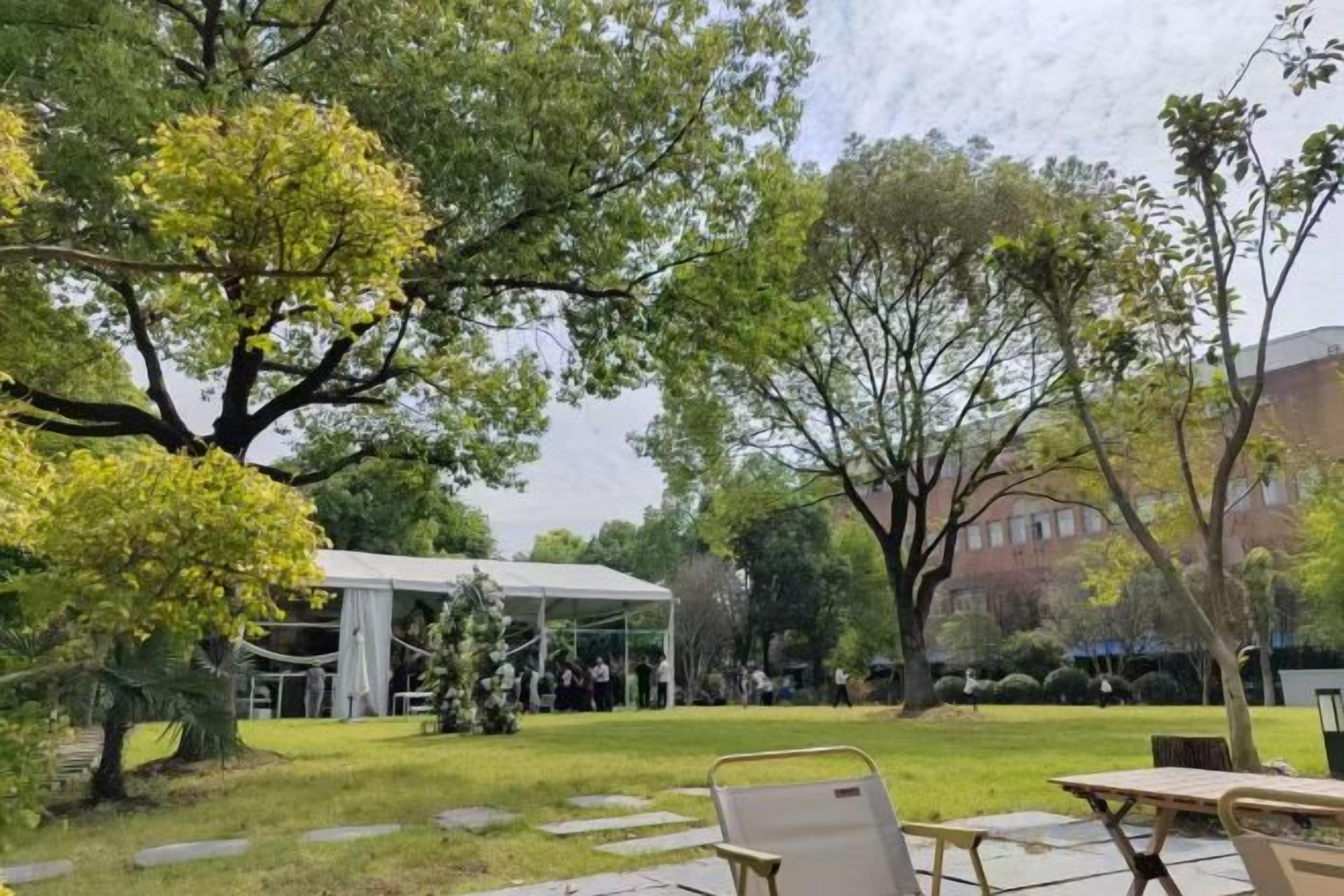 An outdoor area with a covered seating area, a grassy lawn, and trees.