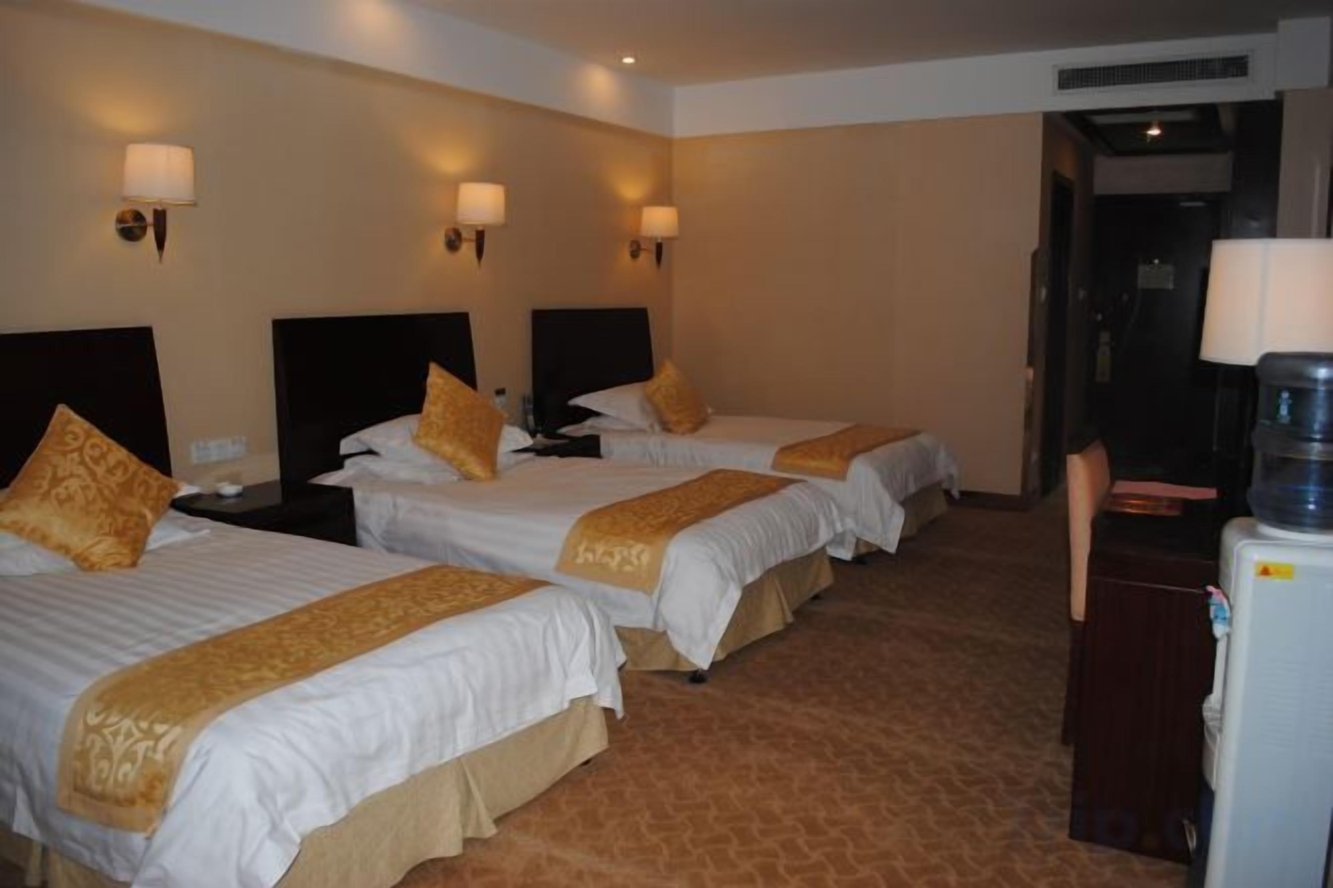 A hotel room with three beds, each with a headboard and a bedside table. There is a water dispenser on the right side of the room.