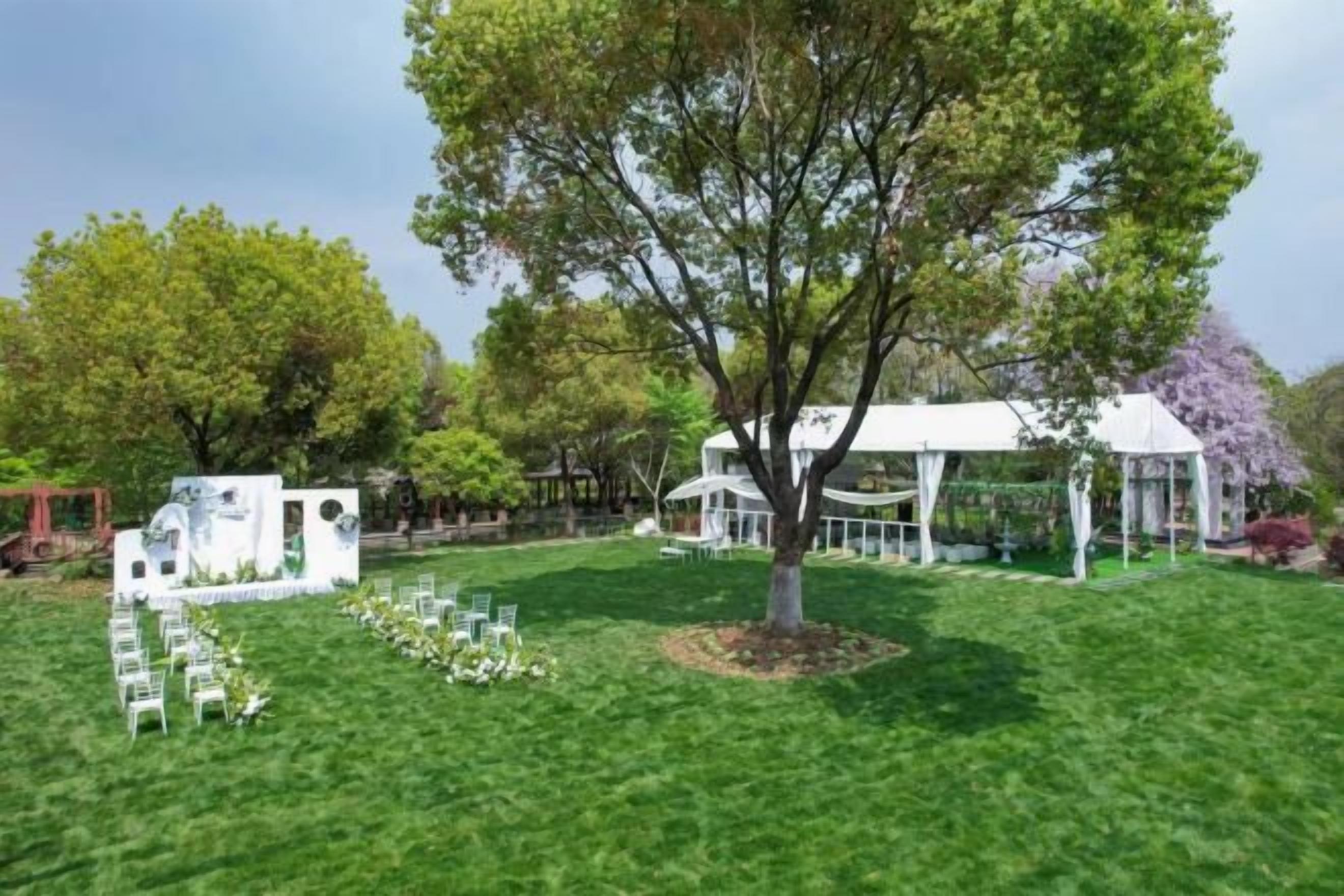 A grassy outdoor area with a white gazebo, a tree, and a white structure with a roof.
