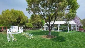 A grassy outdoor area with a white gazebo, a tree, and a white structure with a roof.