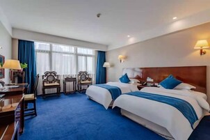 A hotel room with two beds, a desk, chairs, and a large window.