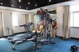 Habitación de hotel con una cinta de correr, equipo de ejercicios y una ventana con cortinas.