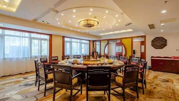 A spacious dining area with a round table and chairs, large windows, and a decorative ceiling.