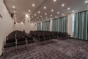 Une salle de conférence avec des rangées de chaises, un sol recouvert de moquette et des rideaux aux fenêtres.