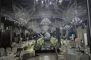 A restaurant with round tables and chairs, a central floral arrangement, and a ceiling adorned with hanging lights.