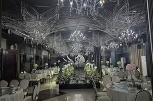 Un restaurante con mesas y sillas redondas, un arreglo floral central y un techo decorado con luces colgantes.