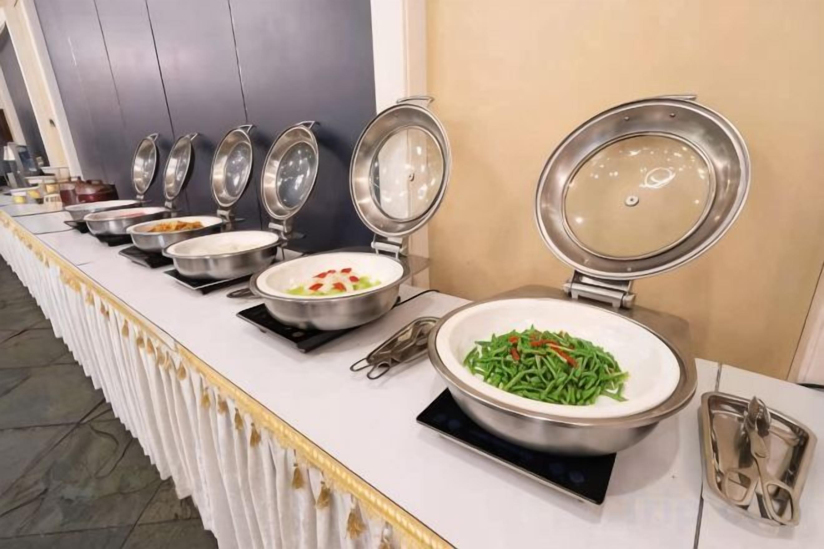 A buffet line with various dishes, including a large bowl of green beans.