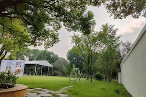 Un patio trasero con césped, un edificio blanco y una terraza de madera.