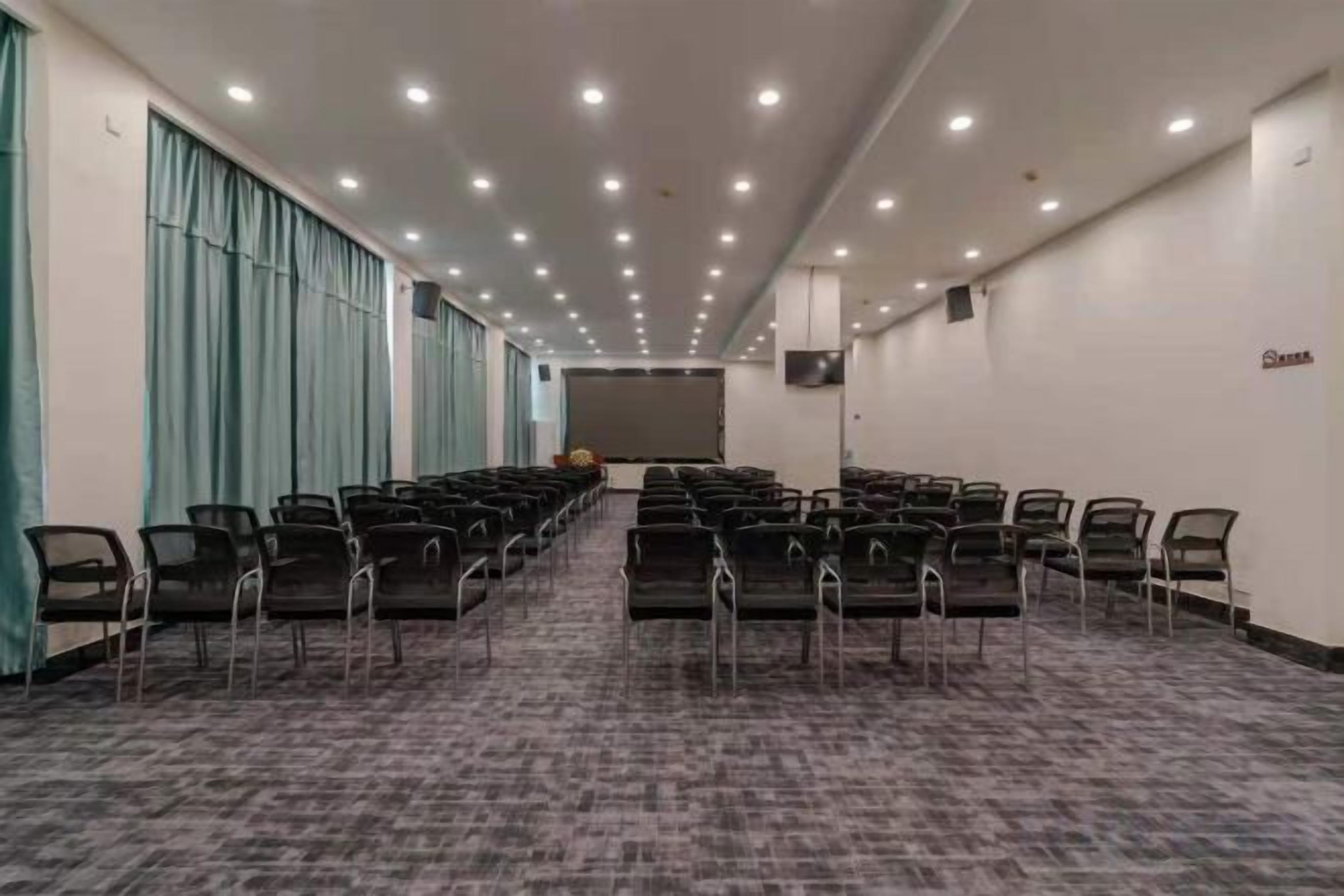 A conference room with rows of chairs, a carpeted floor, and a projector screen.