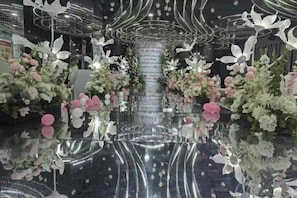 A reflective floor with floral arrangements and a central column.