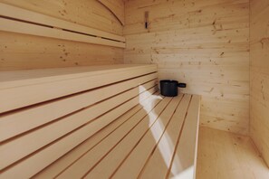 A sauna with wooden benches and a black container, likely for water or towels. - Sona Suites Allgäu: Sauna, Hot Tub, and Alpine Views (Wiggensbach)