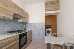 Cocina compacta con estufa a gas, horno y lavadora integrada, con gabinetes de madera y salpicadero de azulejos.