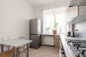 A kitchen with a refrigerator, a stove, a window with curtains, and a potted plant. - Spacious apartment on Białobrzeska Street for 4 guests, in a great location. (Warszawa)