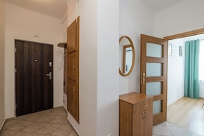 A hallway with a dark wooden door, a wooden cabinet with a mirror, and a glass door leading to another room. - Spacious apartment on Białobrzeska Street for 4 guests, in a great location. (Warszawa)