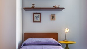 A bed with a headboard, a bedside table with a lamp, and two framed pictures on the wall. - GuestHost - MIRA-MARE Apartment with Parking (Quartu Sant'Elena)