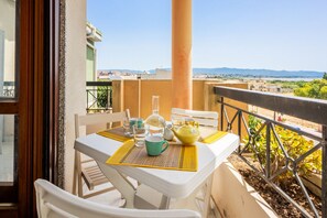 A balcony with a table set for two, chairs, a yellow mat, a green mug, a glass pitcher, and a yellow teapot. - GuestHost - MIRA-MARE Apartment with Parking (Quartu Sant'Elena)