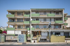 A multi-story residential building with balconies, a gated entrance, and a visible storefront. - GuestHost - MIRA-MARE Apartment with Parking (Quartu Sant'Elena)