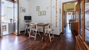 A dining area with a wooden table and chairs, a television, and wall decorations. - GuestHost - MIRA-MARE Apartment with Parking (Quartu Sant'Elena)