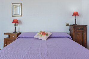 A room with a bed, two nightstands, a wooden cabinet, a mirror, and two red lamps. - GuestHost - MIRA-MARE Apartment with Parking (Quartu Sant'Elena)