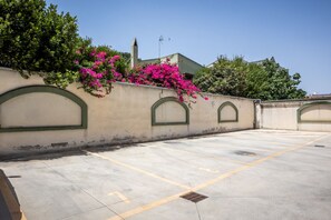 A parking area with a wall adorned with flowering plants and a clear sky. - GuestHost - MIRA-MARE Apartment with Parking (Quartu Sant'Elena)