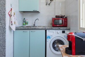 A compact kitchen with a washing machine, a microwave, and a sink. - GuestHost - MIRA-MARE Apartment with Parking (Quartu Sant'Elena)