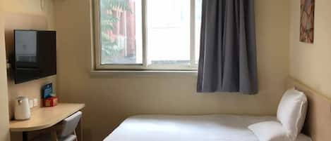 A hotel room with a bed, a desk with a chair, a television, and a window with curtains.