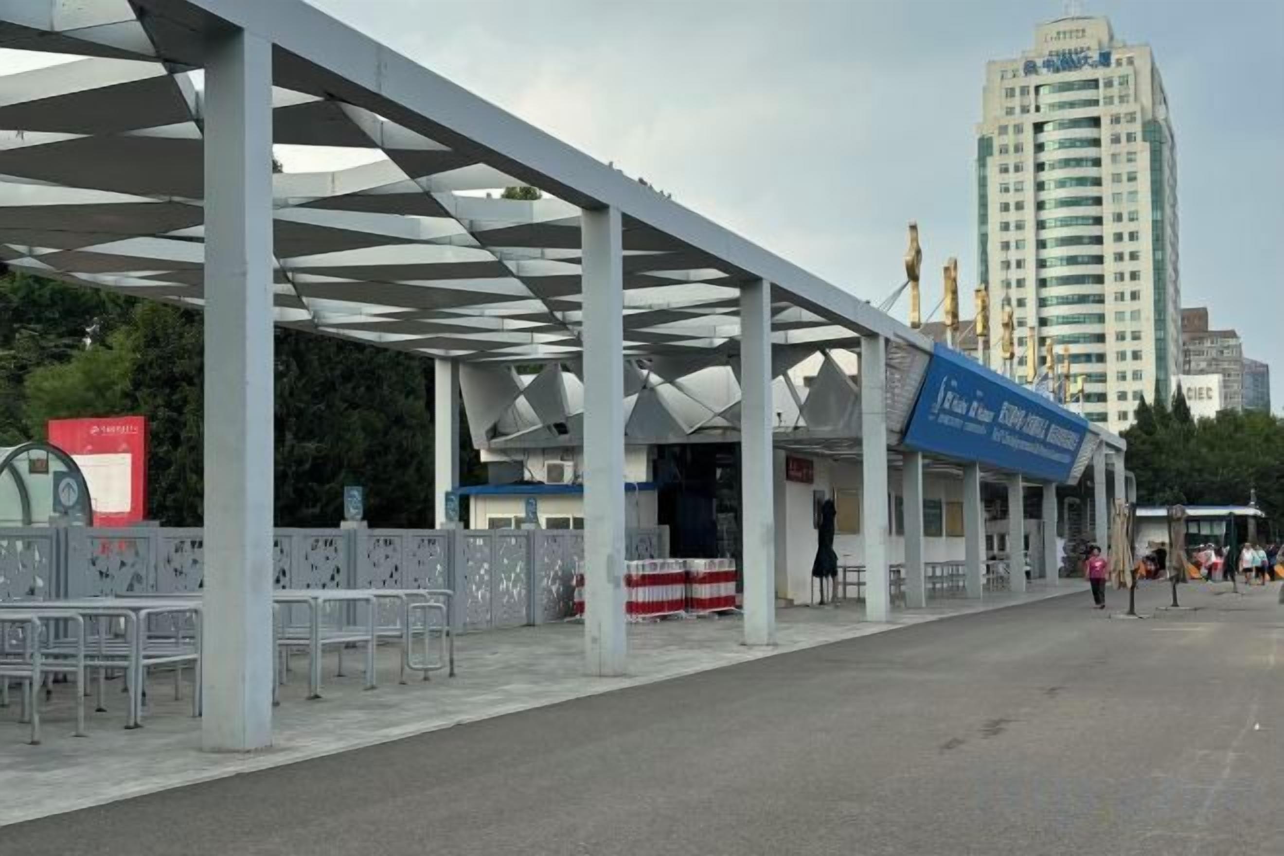 A covered outdoor area with a building in the background, a blue sign, and a fence.