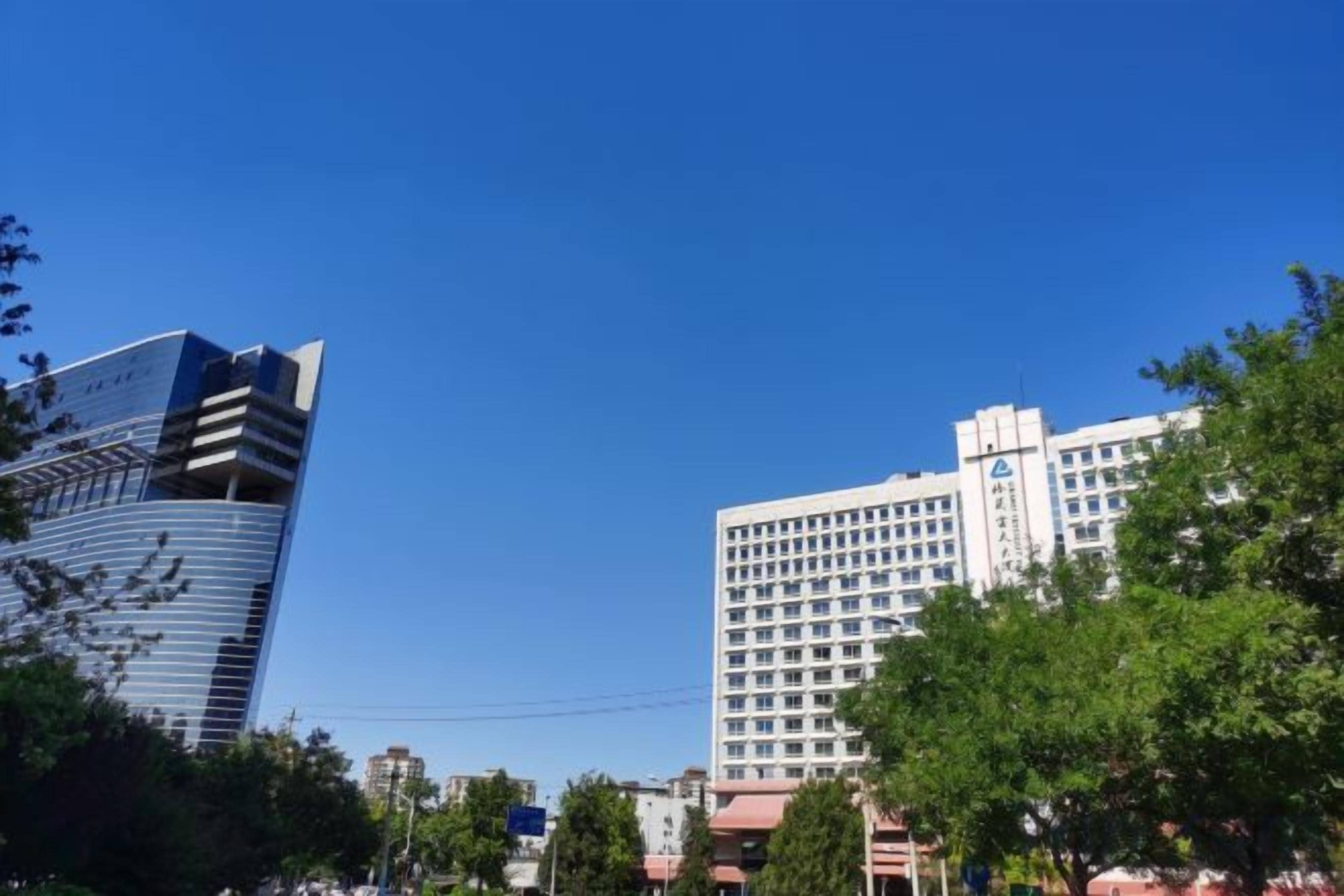A cityscape with modern high-rise buildings, one with a distinctive blue and white facade, and another with a grid-like pattern.