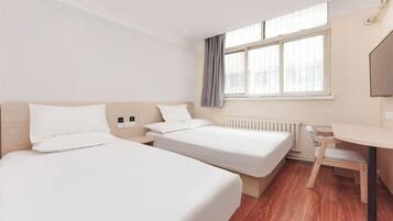 Ett hotellrum med två sängar, ett litet skrivbord och ett fönster med gardiner.