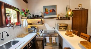 A kitchen with a built-in oven, a toaster, and a coffee maker. There are utensils hanging on the wall and a sink with a faucet. - Casa Sossego in Arraial d'Ajuda (Arraial d'Ajuda)