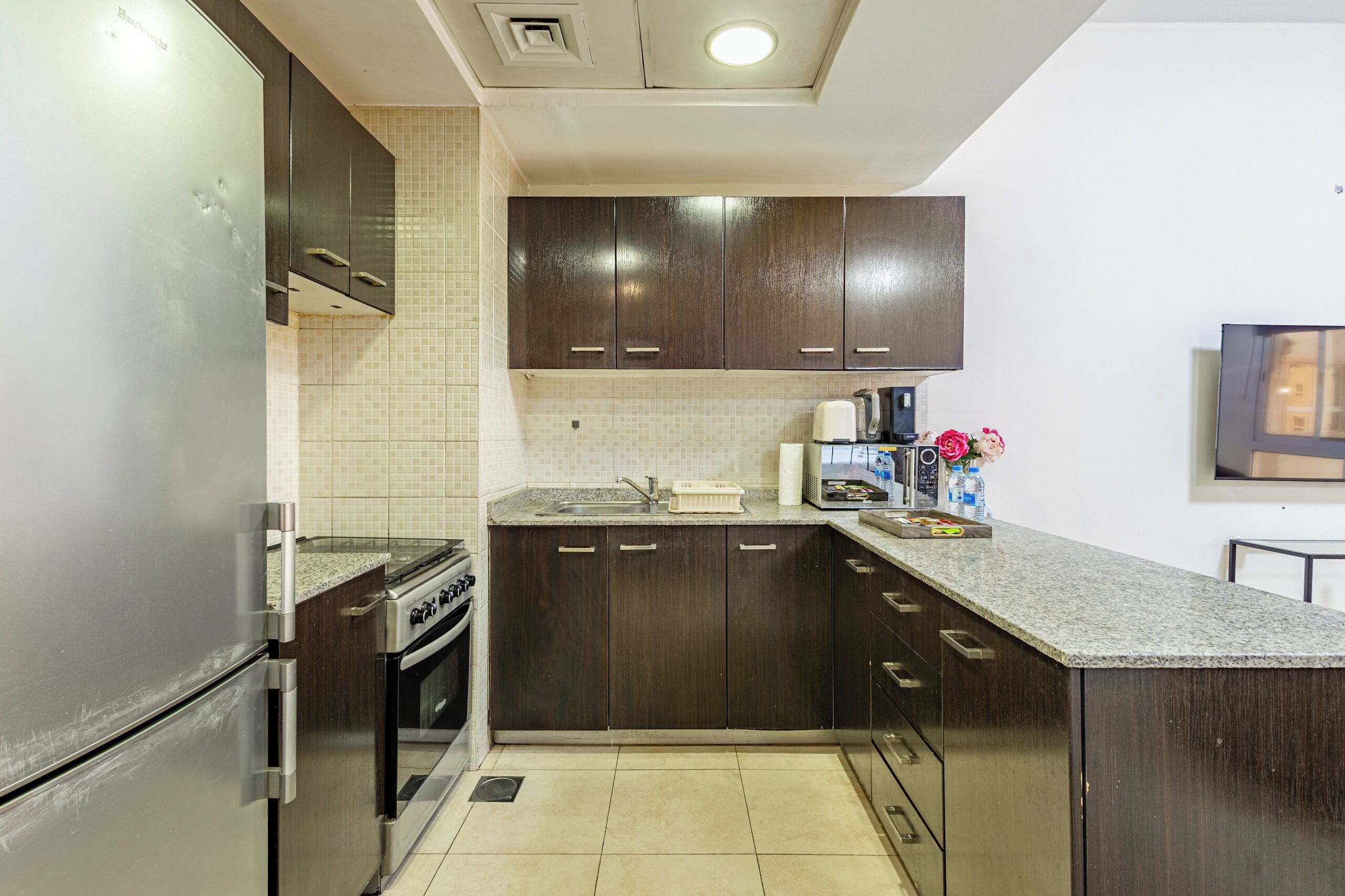 A modern kitchen with dark wooden cabinets, a stainless steel refrigerator, a built-in oven, and a granite countertop.