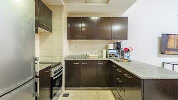 A modern kitchen with dark wooden cabinets, a stainless steel refrigerator, a built-in oven, and a granite countertop.